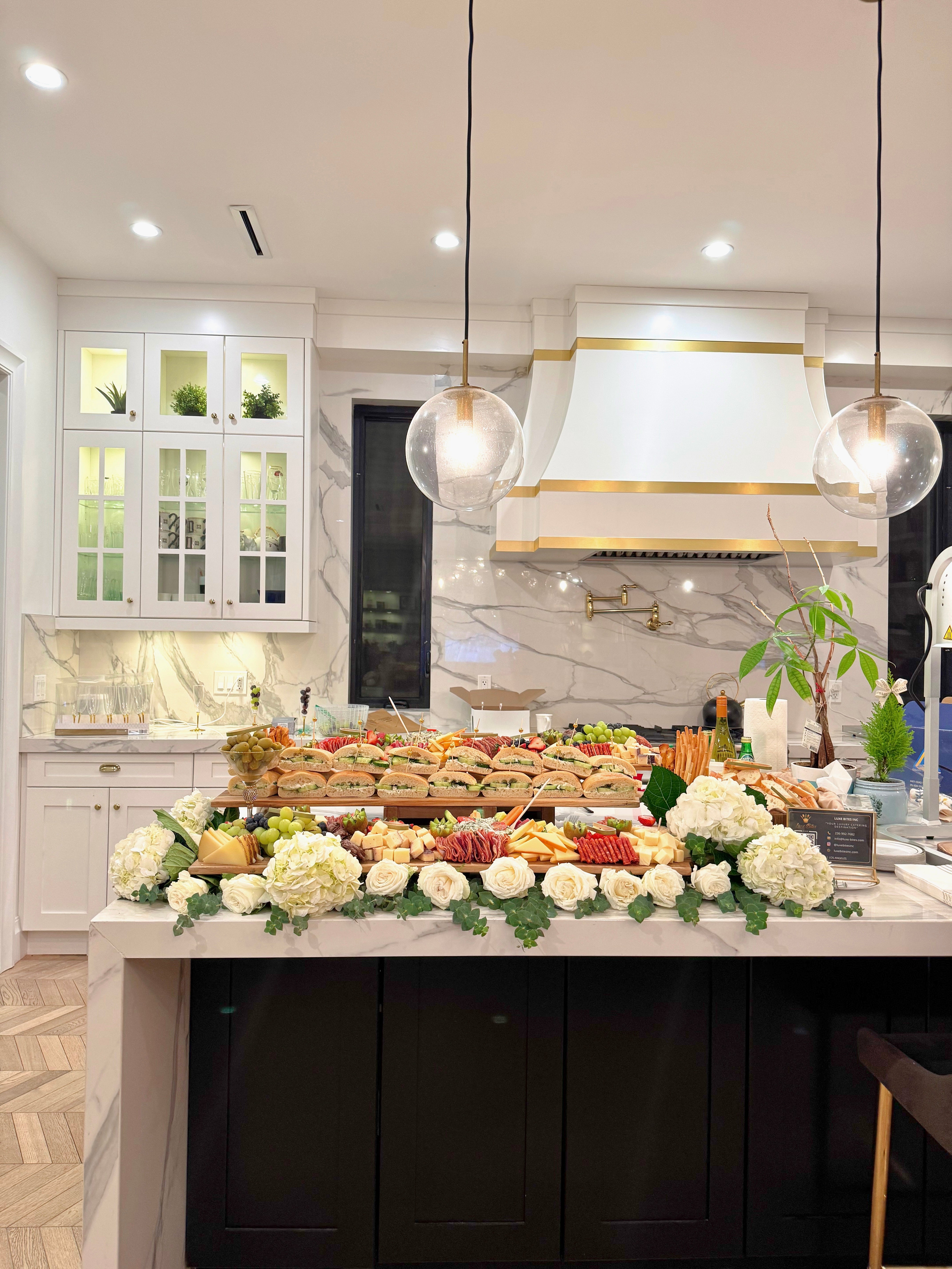 grazing table with sandwiches, charcuterie styled with tiers, floral, and greenery
